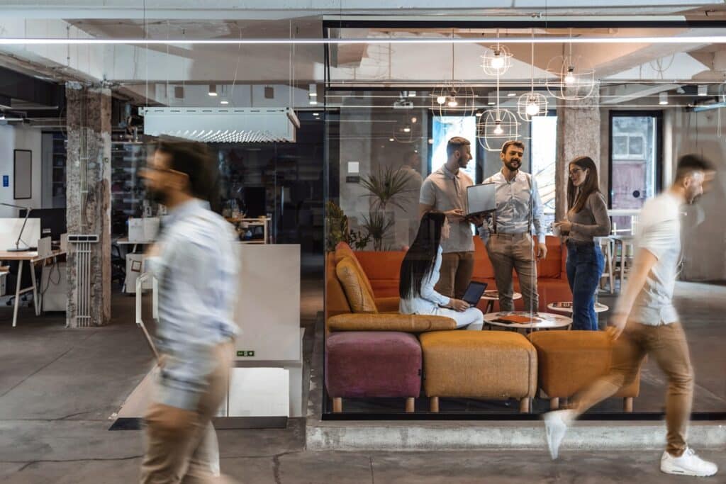 Corporate staff employees working together using computers at coworking, busy workers group walk in motion sitting at desks in modern open space room interior, everyday office rush lifestyle concept