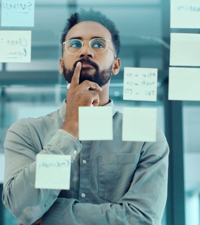 A male in lasses stands in front of a transparent glass board containing post it notes