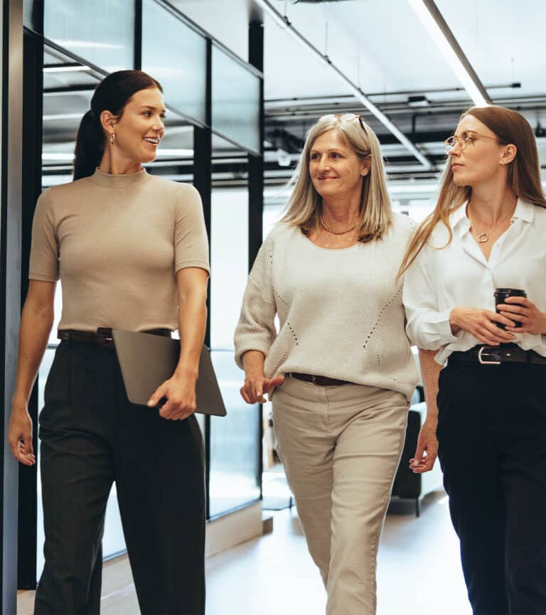 Three female colleagues walk through the office in mid conversation