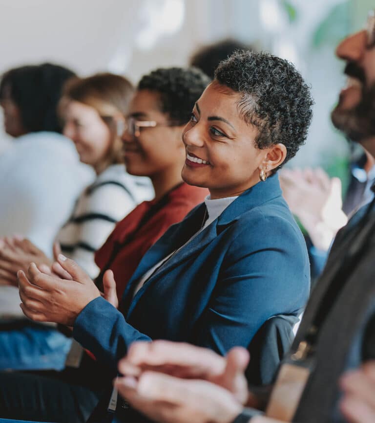 A female sits clapping during a work event