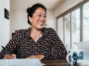 portrait of smiling woman writing with pen at wooden table