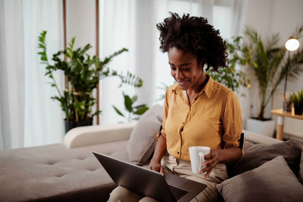 Smiling young woman using laptop, sitting on couch at home