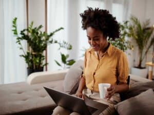 Smiling young woman using laptop, sitting on couch at home