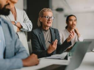 A diverse group of professional individuals engaged in a business meeting within a bright beige office, illustrating teamwork, collaboration, and leadership.