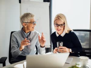 Young business woman looking at laptop when listening to mature coworker